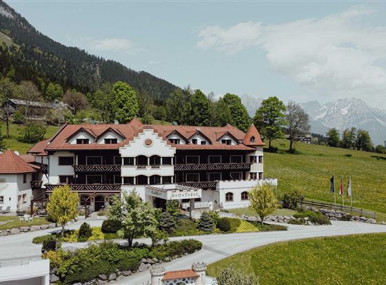 Ein charmantes Hotel inmitten einer malerischen Berglandschaft. Umgeben von grünen Wiesen und Bäumen strahlt es eine einladende Atmosphäre aus.