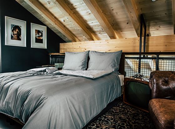 Ein modernes Schlafzimmer mit einem großen Bett und grauer Bettwäsche. Die Holzbalken und die stilvolle Einrichtung schaffen eine gemütliche Atmosphäre.