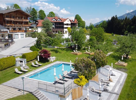 Ein schöner Außenbereich mit einem Pool und Liegen. Im Hintergrund sind malerische Berge und grüne Wiesen zu sehen.