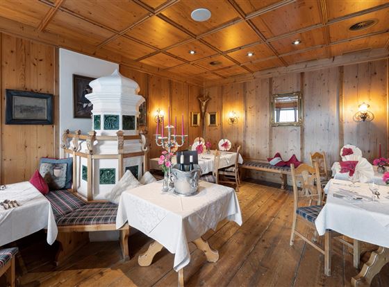 Ein gemütliches Restaurant mit Holzwänden und elegant eingedeckten Tischen. In der Mitte steht ein traditioneller Kachelofen.