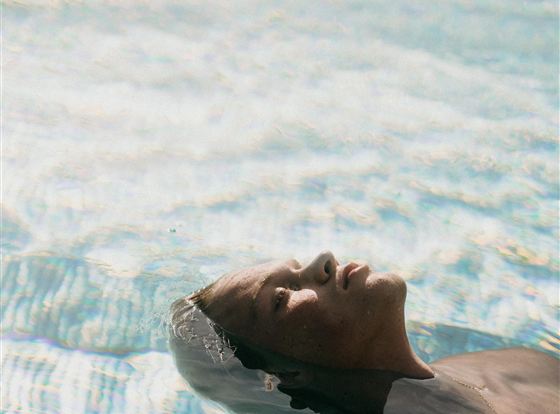 Ein Mann liegt entspannt auf dem Wasser in einem Pool. Die sanften Wellen spiegeln das Licht wider und schaffen eine ruhige Atmosphäre.