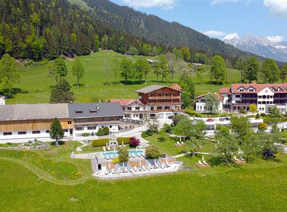Un hotel pintoresco en el campo, rodeado de montañas y prados. El área exterior cuenta con una piscina y jardines bien cuidados.