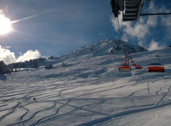 Ein schneebedeckter Hang mit Skizügen und einer sonnigen, klaren Himmel. Im Hintergrund ist ein Skilift zu sehen.
