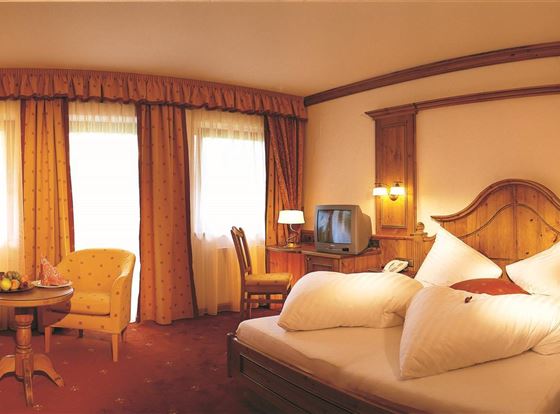 Een gezellige hotelkamer met een groot bed en kleurrijke gordijnen. Er is een zithoek met een tafel en een televisie in de kamer.