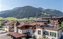 A beautiful hotel amidst a green landscape with mountains in the background. The terraces are equipped with loungers and invite relaxation.