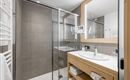 A modern bathroom with a glass shower and a wooden sink. The room is bright and clean with neutral colors.