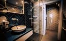 A modern bathroom with blue tiles and an elegant washbasin. The shower is open and the space is well-lit.