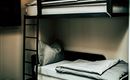 Ein modernes Schlafzimmer mit einem Etagenbett und einem Schlafsofa. Die Wände sind hell und die Beleuchtung ist warm.
