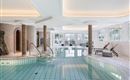 An elegant indoor pool with clear blue tiles and relaxing loungers. Large windows let in plenty of daylight.
