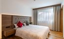 A cozy bedroom with a large bed and decorative pillows. Bright walls and wooden flooring create an inviting atmosphere.