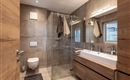 A modern bathroom with a glass shower cabin and wooden shelves. The walls are in neutral colors, and there are large windows for natural light.