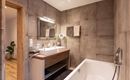 A modern bathroom with a freestanding bathtub and a double sink. The walls are designed in a concrete look, and a large mirror adds style.