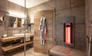 A modern bathroom with wood and concrete elements. There is a sink, a mirror, and an infrared heat lamp.