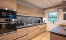 A modern kitchen with wooden furniture and a gray countertop. It is bright and well-equipped with modern appliances.