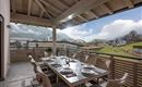 A cozy terrace with a large dining table and a view of the mountains. The surroundings are green and the clouds create a relaxed atmosphere.
