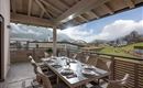 A spacious terrace with a large dining table and stylish chairs. In the background, there are mountains and a picturesque landscape.