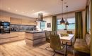 Modern kitchen with wooden cabinets and a cooking island. An inviting dining area with green chairs and soft lighting.