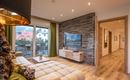 A modern living room with a cozy sofa and a television. Large windows offer a view of a balcony and plenty of daylight.