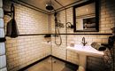 A modern bathroom with white tiles and a glass shower. On the wall, it says "THE BEATLES," and there are towels as well as an elegant washbasin.