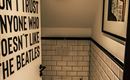 A modern bathroom with white tiles and a minimalist design. A sign on the wall alludes to the Beatles.