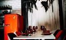 A modern dining room with a striking red refrigerator. At a table with black and red chairs, stylish wine glasses and plates are decorated.