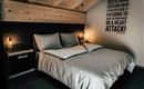 A modern bedroom with a cozy bed and a wooden ceiling. A humorous quote hangs on the wall, catching attention.