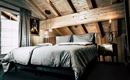 A stylish bedroom with a large double bed and wooden ceilings. The room has large windows and a cozy atmosphere.