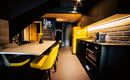 A modern kitchen with a yellow cooler and stylish furniture. The room has warm lighting and an inviting atmosphere.