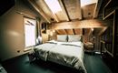 Ein modernes Schlafzimmer mit einem Doppelbett und Holzdecke. Große Fenster sorgen für viel Tageslicht.