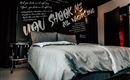 Ein modernes Schlafzimmer mit einem großen Bett und einer stilvollen Wandgestaltung. Die Wand ist mit auffälligen Texten in verschiedenen Schriftarten verziert.