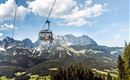 A cable car travels over the impressive mountains and valleys. The sky is blue with some clouds.