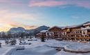 A cozy mountain landscape with a snowy hotel and a picturesque sunset. The surroundings are tranquil and surrounded by winter trees.