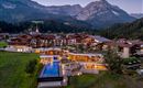 A picturesque hotel in the mountains with modern architecture and a beautiful pool. The surroundings consist of green meadows and majestic mountains.