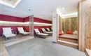 A modern relaxation room with comfortable loungers and wooden details. The walls are painted in warm shades of red, creating an inviting atmosphere.