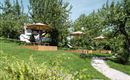 A green garden area with sun umbrellas and loungers. The space is surrounded by trees and offers an inviting, quiet place to relax.