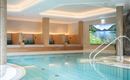 A relaxing wellness area with a swimming pool and cozy loungers. On the wall, there is a screen displaying a landscape image.