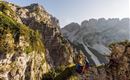 A stunning mountain landscape with steep rocks and green forests. Two hikers enjoy the view of the surrounding peaks.