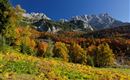 A picturesque mountain landscape in autumn with colorful deciduous trees. In the background rises an impressive mountain range under a clear blue sky.