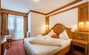 A cozy hotel room with wooden decor and a large bed. There is a table, a chair, and a window with curtains.