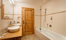 A modern bathroom with a wooden door and large mirrors. There is a bathtub, two sinks, and a shower.