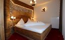 A cozy bedroom with a wooden bed and decorative pillows. The warm light accents and the wooden paneling create an inviting atmosphere.