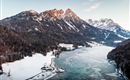 A charming landscape with snow-covered mountains and a frozen lake. The sky is clear and the colors of the sunset are visible.