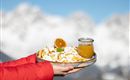 A plate with delicious, fried dough pieces and a slice of orange, served with a glass of juice. In the background, snow-covered mountains can be seen.