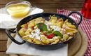 A delicious Kaiserschmarrn, served in a pan, with powdered sugar, fresh berries, and mint. Accompanied by a bowl of applesauce.