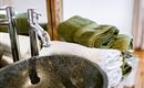 A modern stone sink with shiny faucets. On it lie clean, green, and white towels.