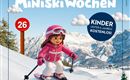 A girl on skis in pink clothing is skiing down a slope. In the background, there are snow-covered mountains and a blue sky with clouds.