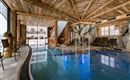 An elegant indoor pool in a wooden building with large windows. Comfortable loungers and natural elements create a relaxing atmosphere.