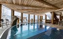 An elegant indoor pool in a rustic wooden building. Large windows offer a view of the snow-capped mountains.