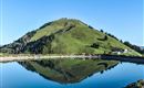 A beautiful mountain with green meadows and pine trees. The clear sky is reflected in the calm water of a pond.