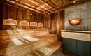 A quiet sauna with a wooden bench and warm light. The walls are clad in wood and a copper bowl hangs from the ceiling.